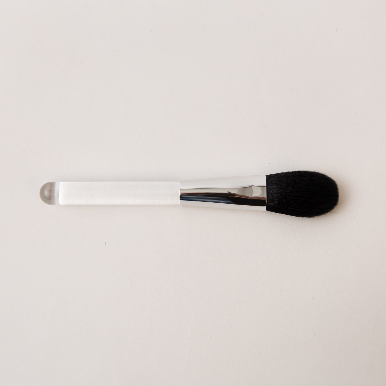 Makeup brush with black bristle head and silver handle on a light gray background