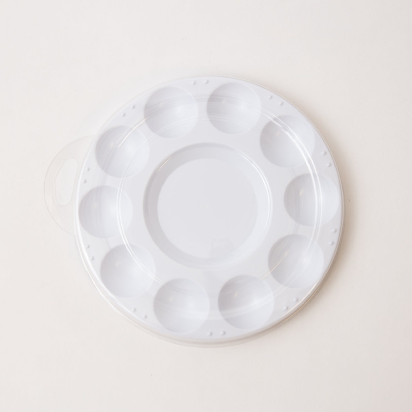 White plastic mixing paint palette tray with multiple compartments on a light beige background
