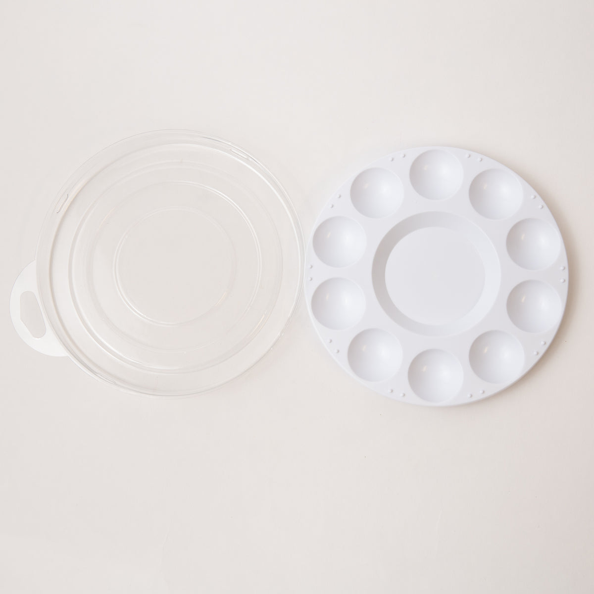 White plastic mixing palette plate with a matching lid on a light beige background