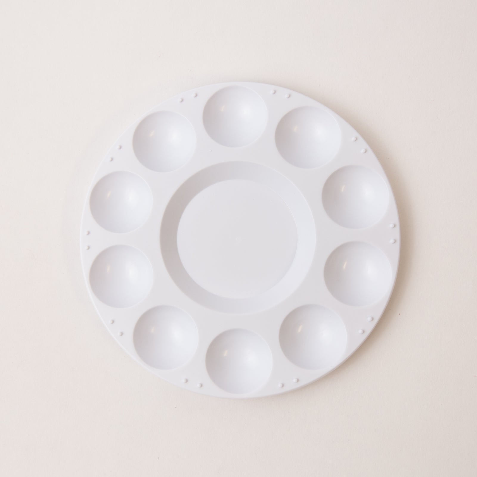 White round paint palette with multiple compartments on a beige background