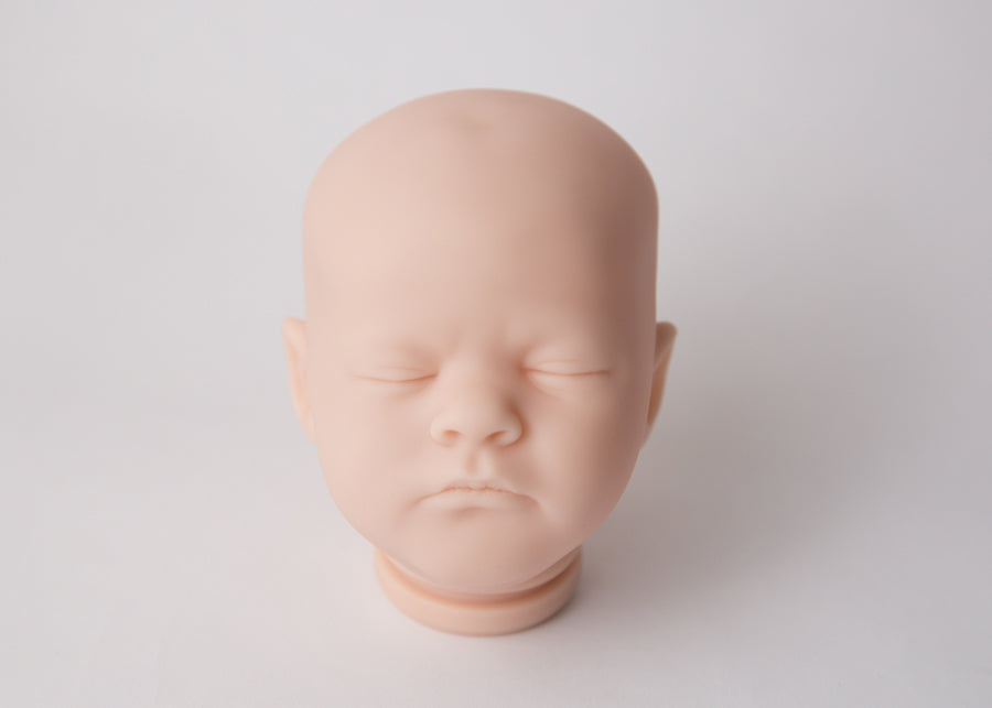 Baby doll head with closed eyes on a light gray background